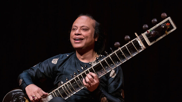 Tabla maestro Nishat Khan playing an instrument against a dark background