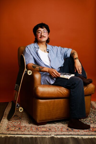 Miguel Fernandez seated in brown leather arm chair with a skateboard leaning against the chair.